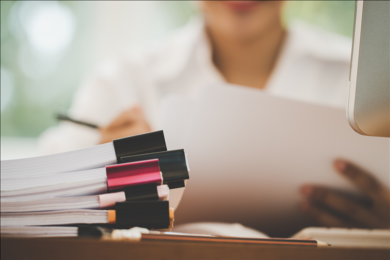woman sitting at desk with stacks of paper held together by binder clips on desk